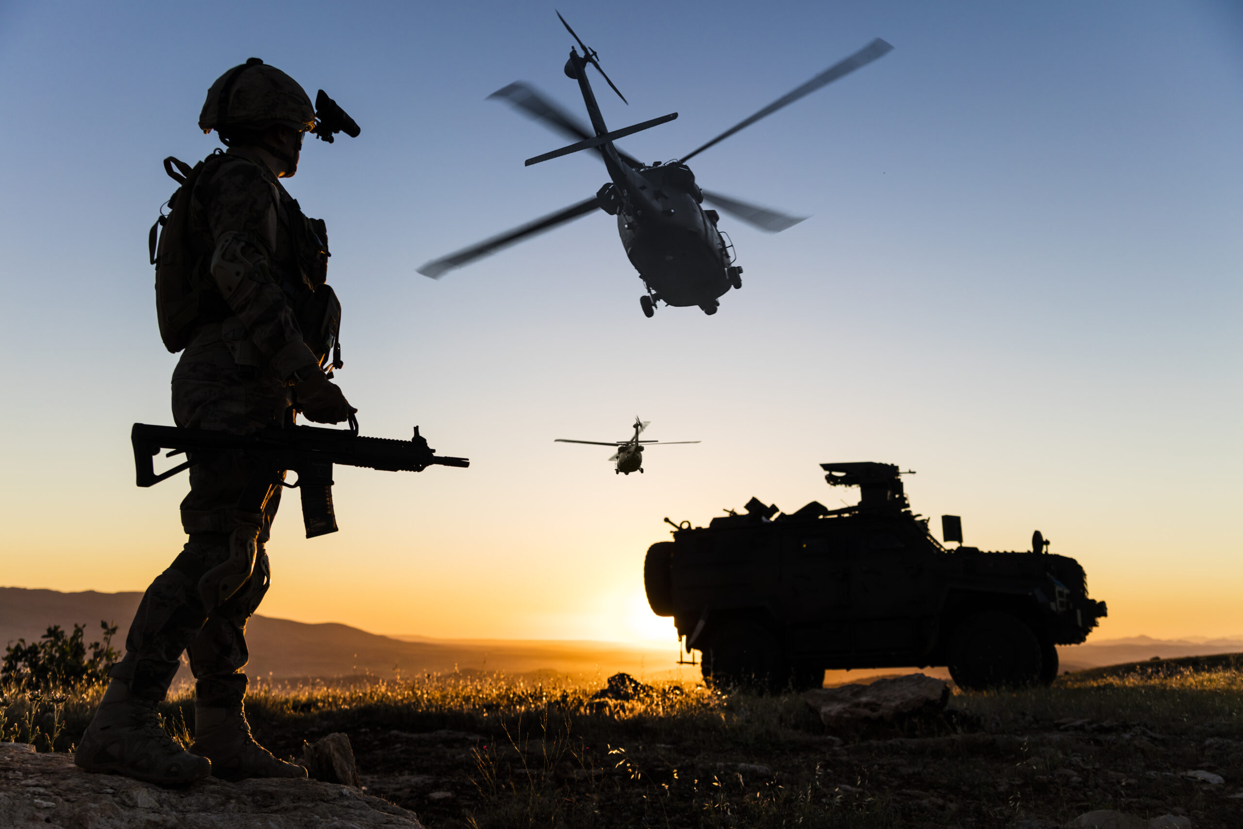 Silhouettes of a soldier, helicopters and an armored vehicle at sunset